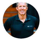 A smiling man in a black polo shirt standing in front of wooden steps.